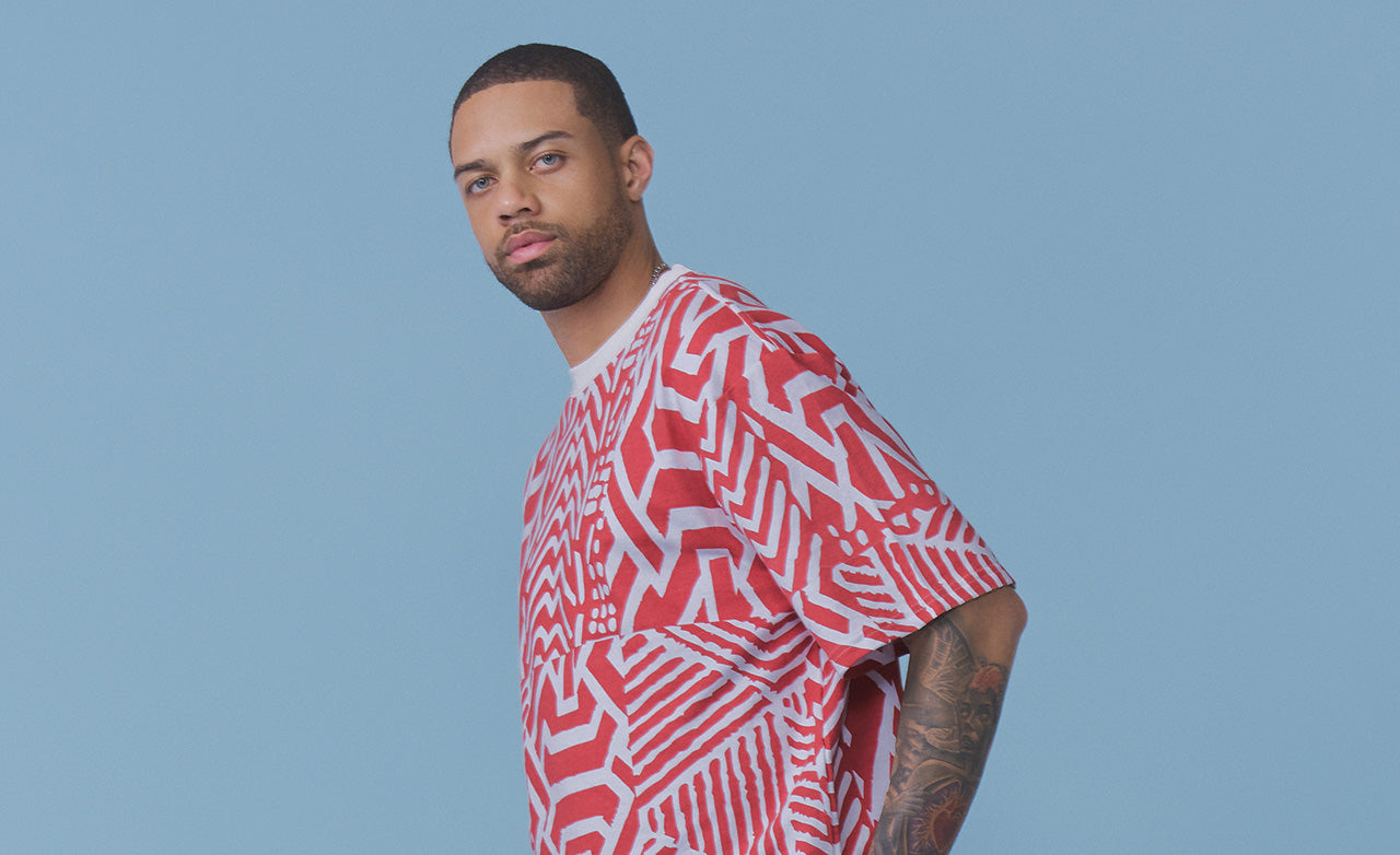 A man wearing a red and white geometric patterned t-shirt, photographed against a solid light blue background.