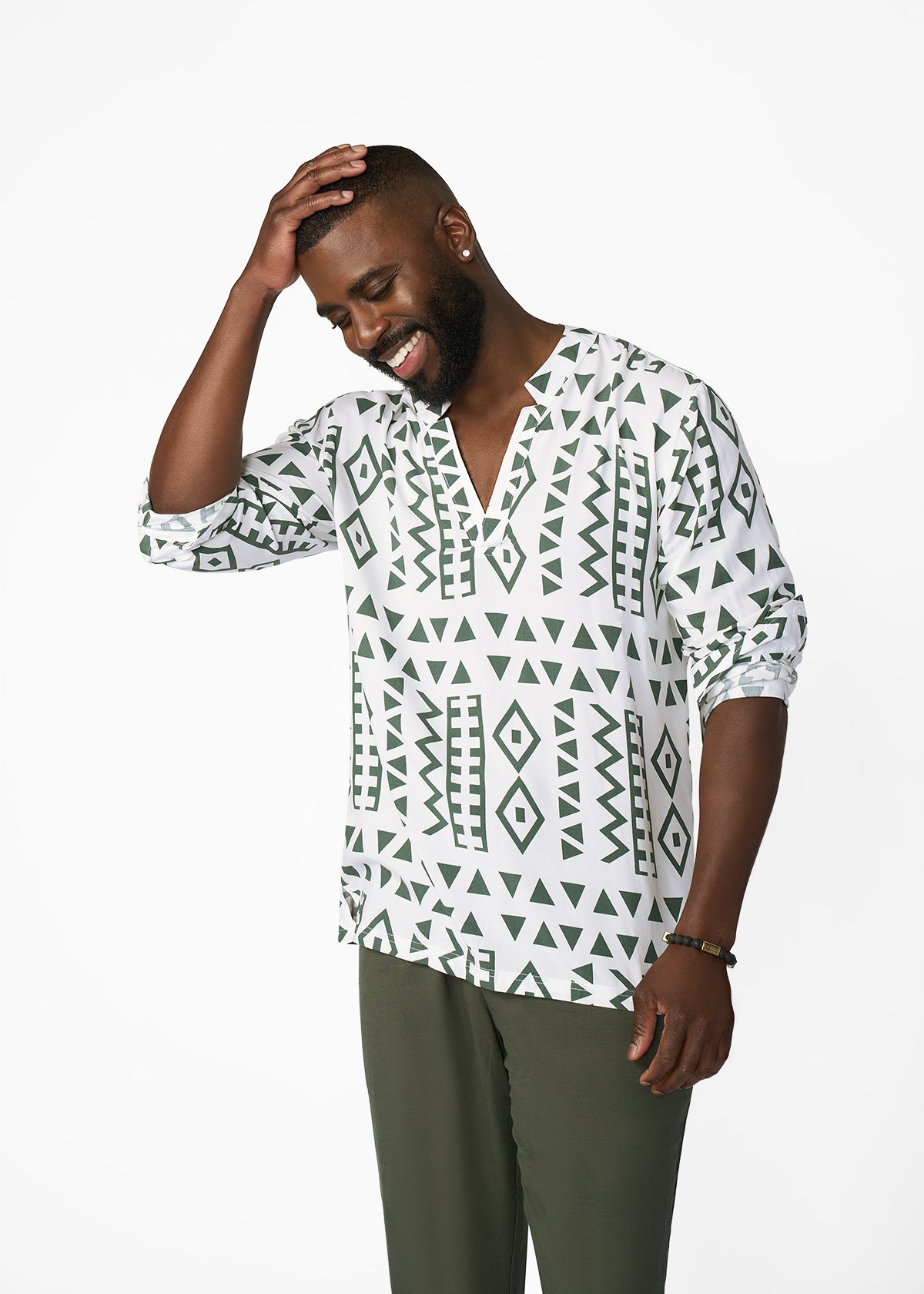 A man wearing a white long-sleeve button-up shirt with a dark green geometric tribal pattern, paired with olive green trousers, posing against a solid white studio background.