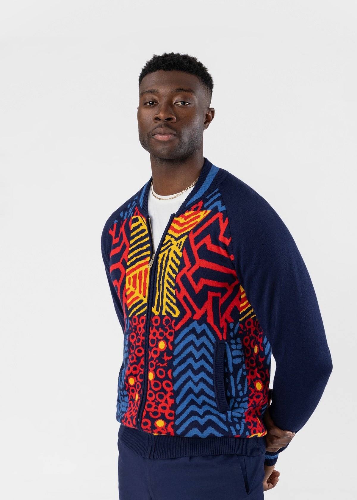 Three quarter view of Togo mens African print zip up sweater in poppy navy multipattern worn by a model on a light gray background