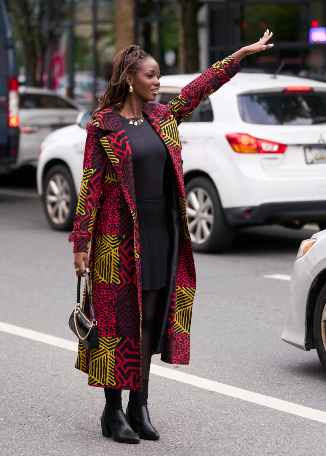 Woman in a african patterned trench coat standing on a street with cars in the background