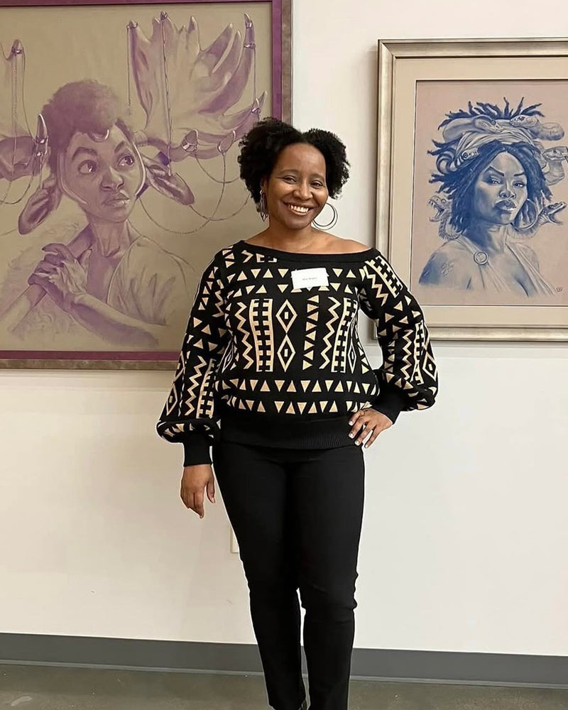 Front view of Hiba Women’s African Print Off-Shoulder Sweater showcasing tan and black tribal print on a model in an art gallery