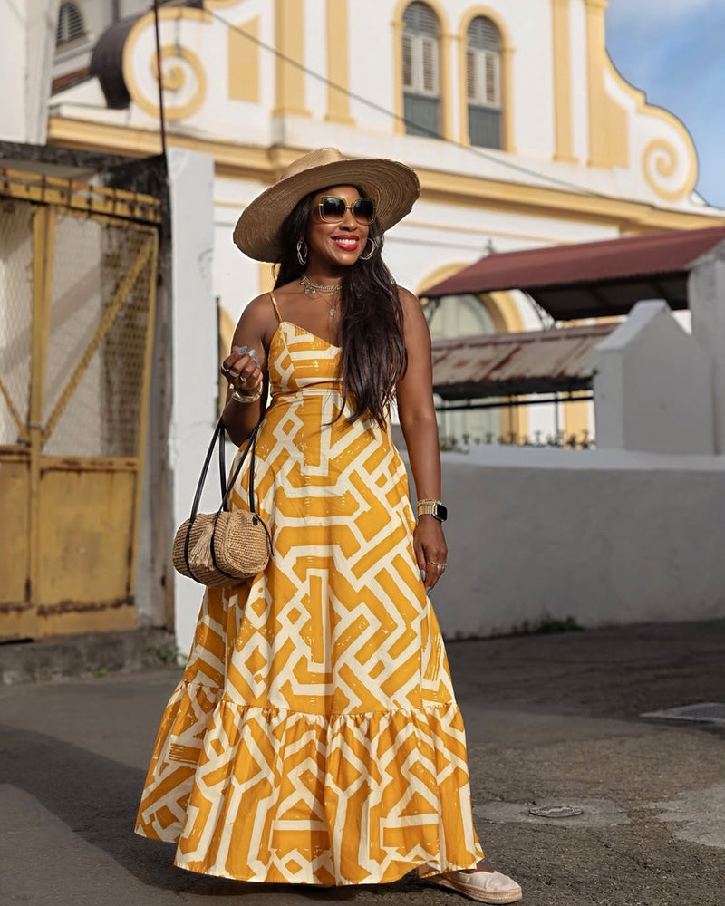 Front view of Oneyka maxi dress showcasing gold cream African print and tiered hem with an outdoor architectural background