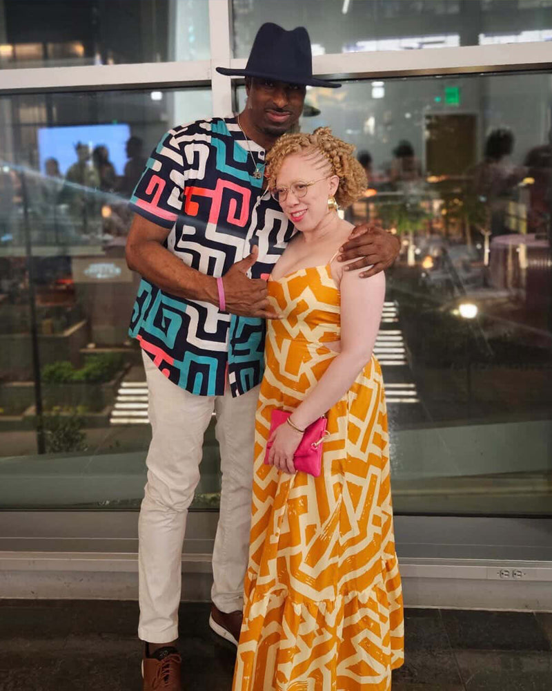 Woman wearing a gold and cream patterned maxi dress poses with a man indoors