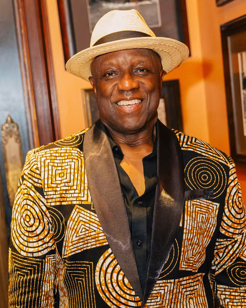 Man wearing a black and brown geometric African print blazer and hat indoors