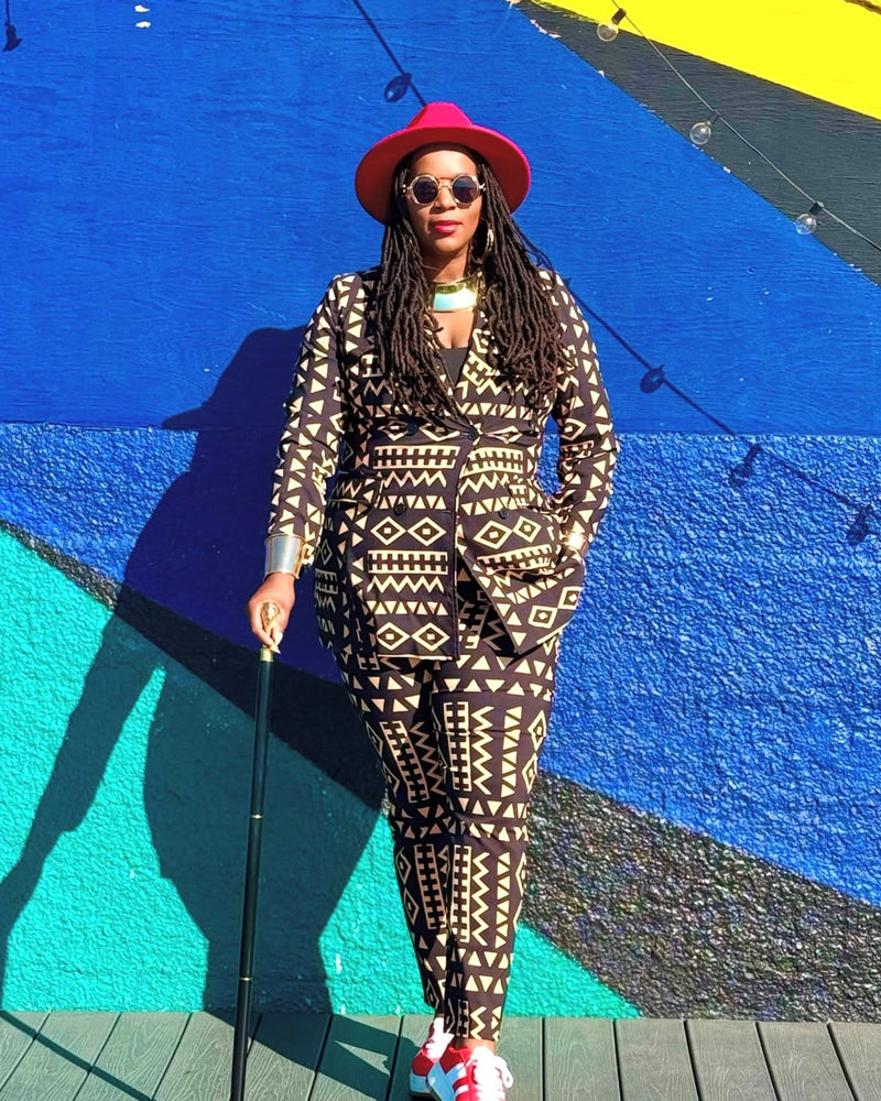 Front view of Uyai women’s tan and black tribal print blazer on model, showing geometric pattern against a colorful mural