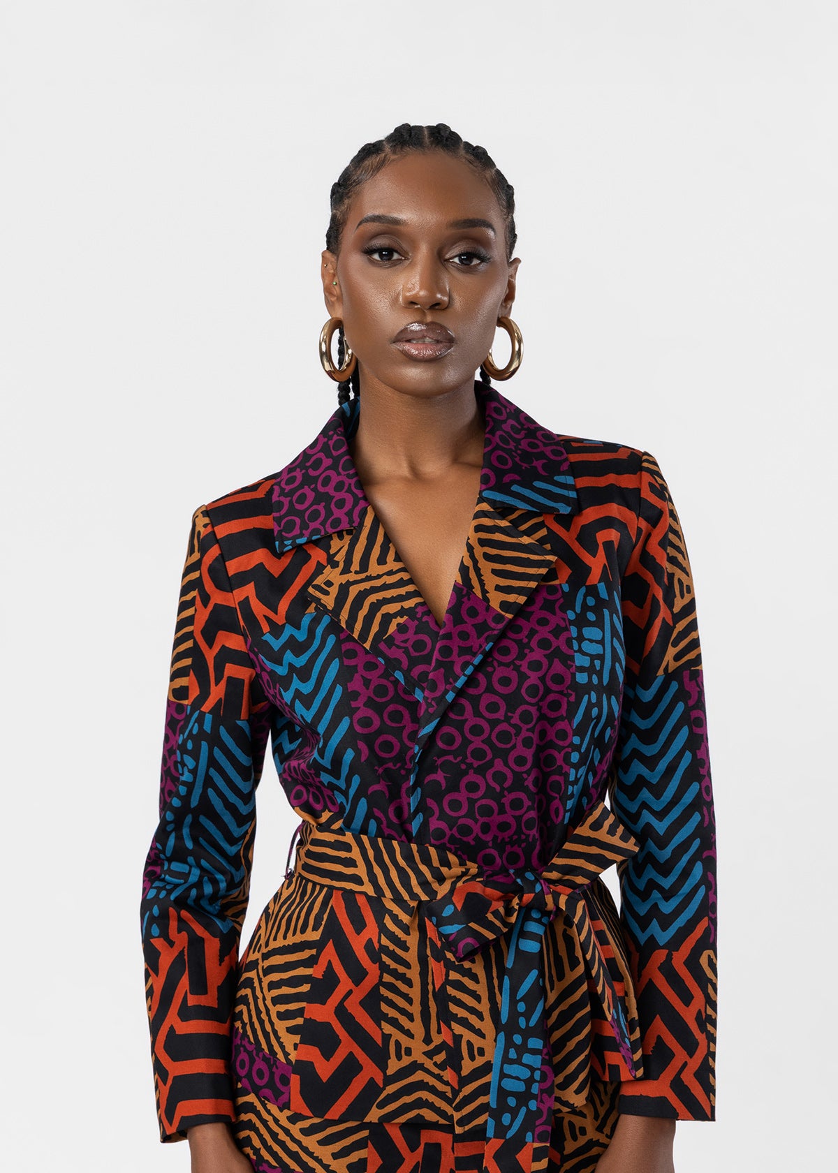 A model wearing a long-sleeve wrap blazer and matching skirt featuring a vibrant multicolor geometric and abstract pattern in orange, blue, purple, and black, set against a plain light gray background.