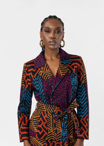 A model wearing a long-sleeve wrap blazer and matching skirt featuring a vibrant multicolor geometric and abstract pattern in orange, blue, purple, and black, set against a plain light gray background.