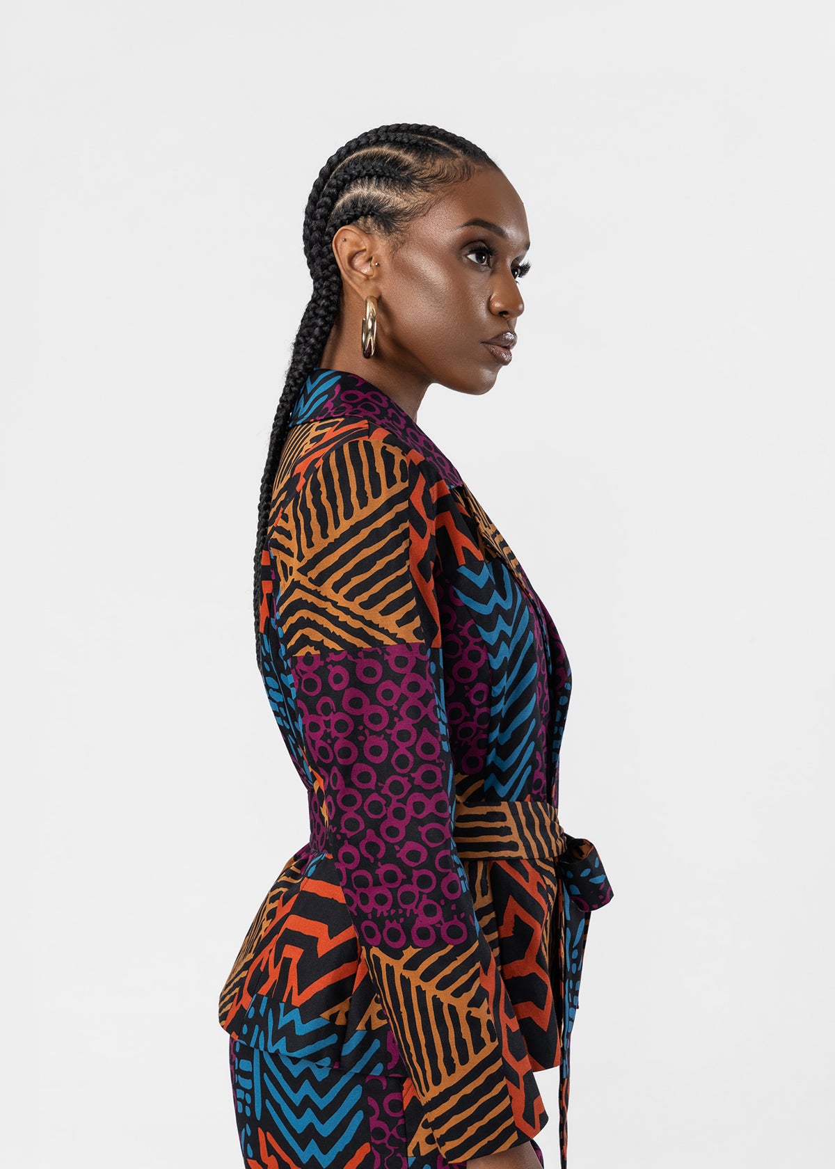 A woman in profile wearing a colorful geometric print wrap jacket with purple, orange, blue, and black patterns, set against a plain light gray background.