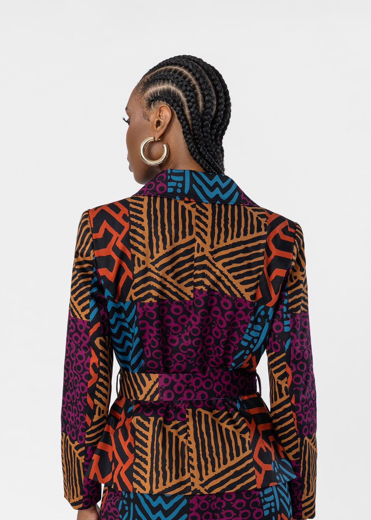 A woman shown from the back wearing a long-sleeve belted blazer with a vibrant multicolor geometric and tribal pattern in orange, black, purple, and blue, set against a plain light gray background.