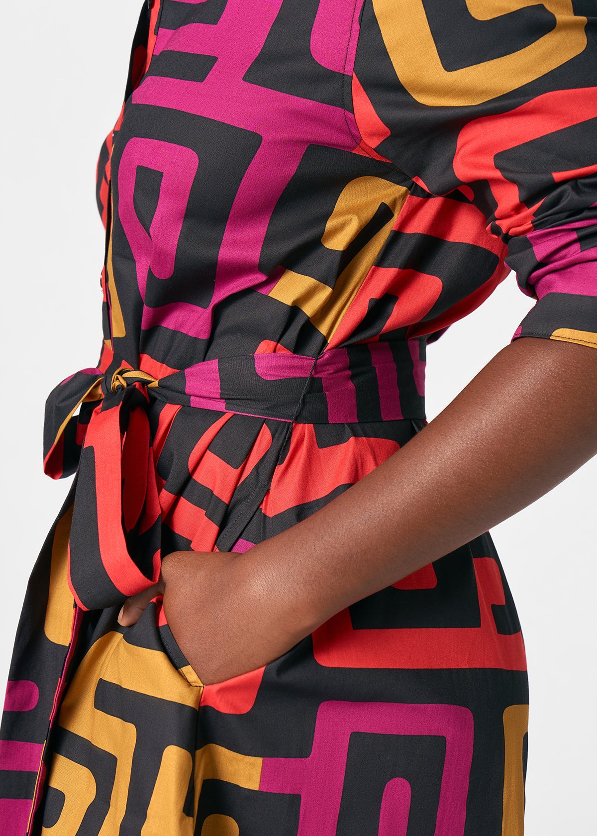 Side view of Kianga women’s African print shirt dress with waist tie, pocket, three-quarter sleeve and bold black, berry and gold Kuba geometric print on pale gray background