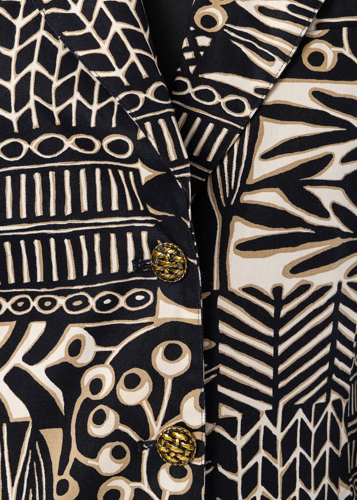 Close-up of a patterned blazer with a black and beige abstract botanical print and decorative gold buttons.