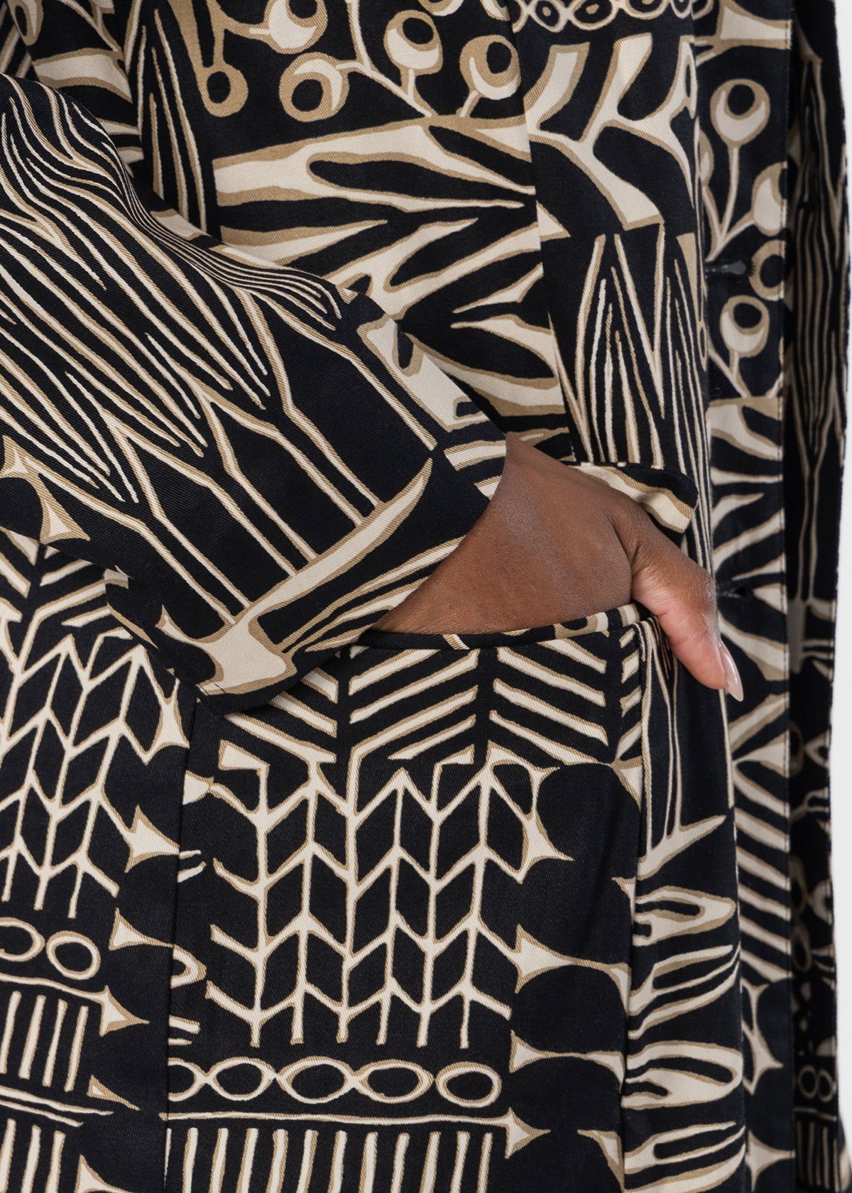 Close-up of a black and beige patterned garment with a hand tucked into a front pocket, showing a bold abstract print and soft fabric texture.