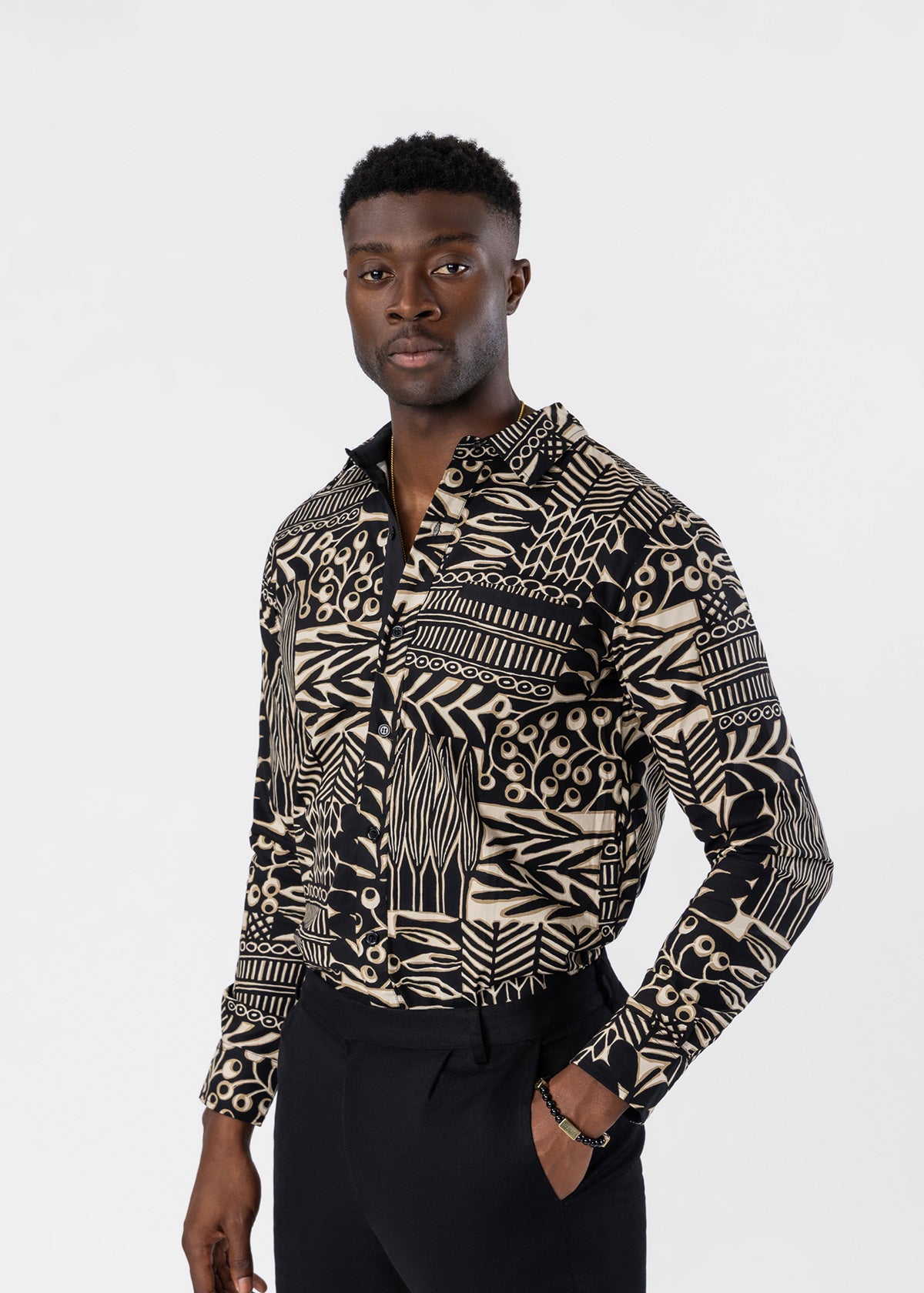 A man wearing a long-sleeve button-up shirt with a bold black and beige geometric tribal pattern, posed against a solid light gray background.