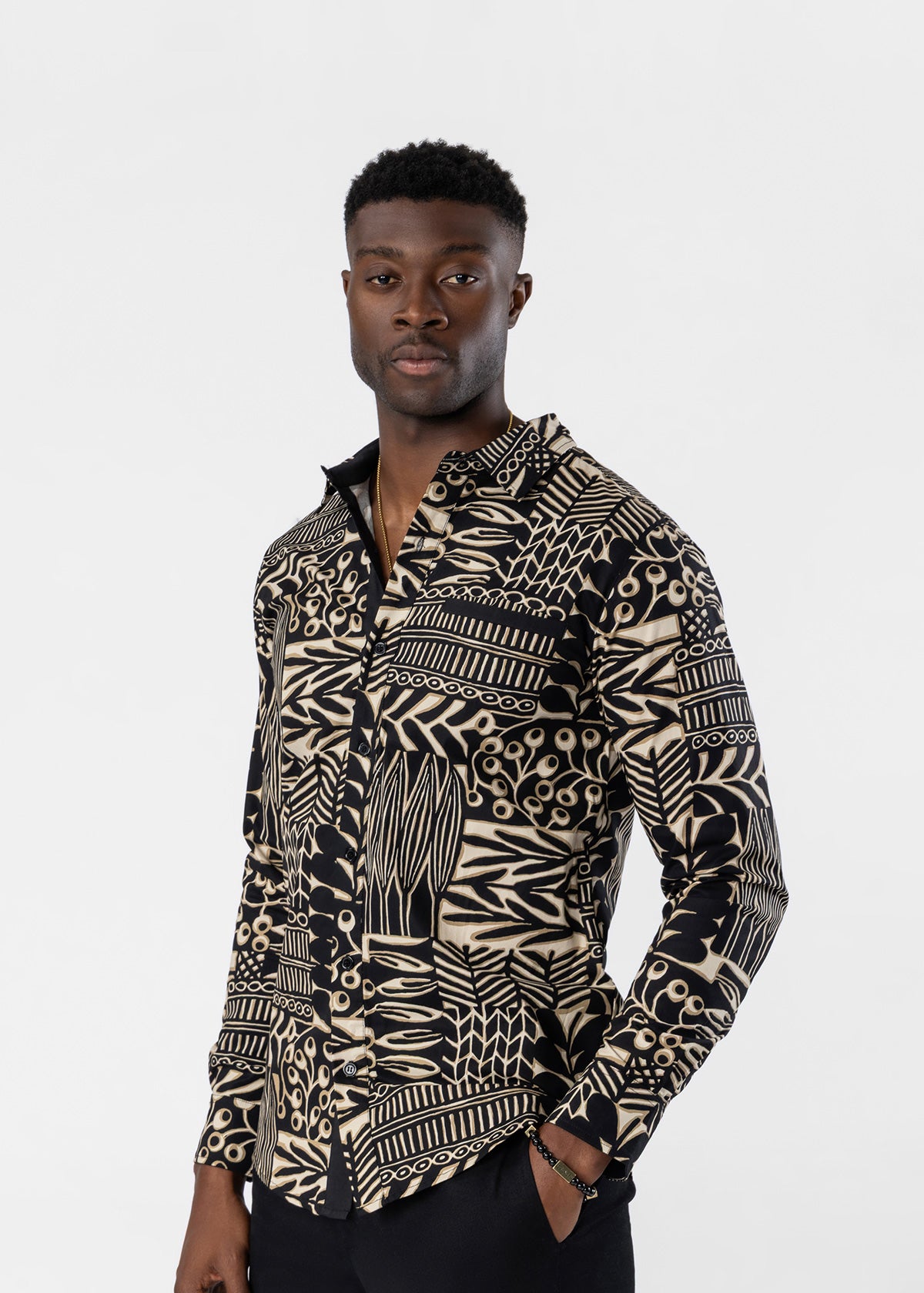 A man wearing a long-sleeve button-up shirt with a bold black and beige geometric tribal pattern, posed against a solid light gray background.