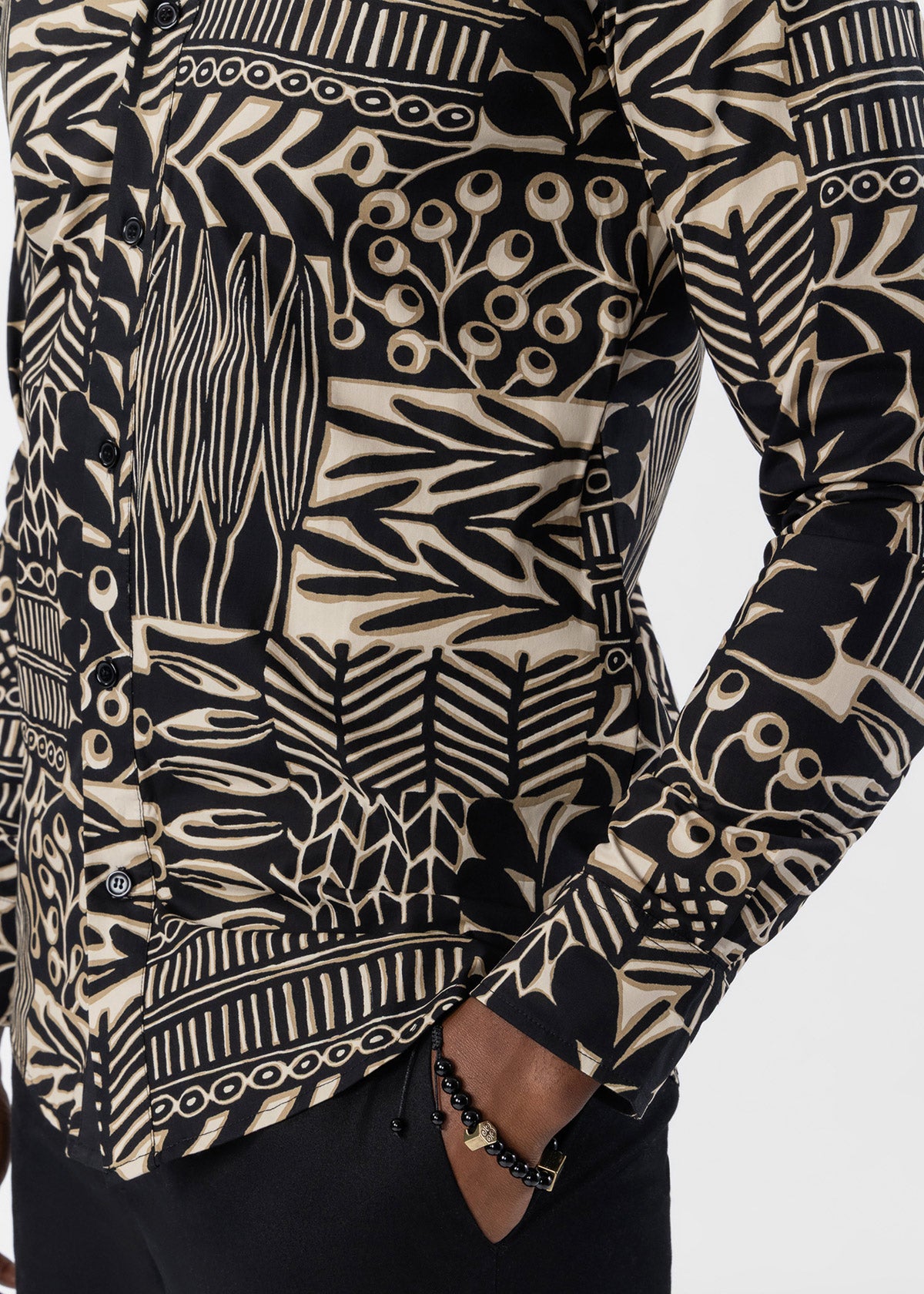 A close-up of a long-sleeve button-up shirt with a bold black and beige botanical block-print pattern, worn by a model whose hand is in their pocket.