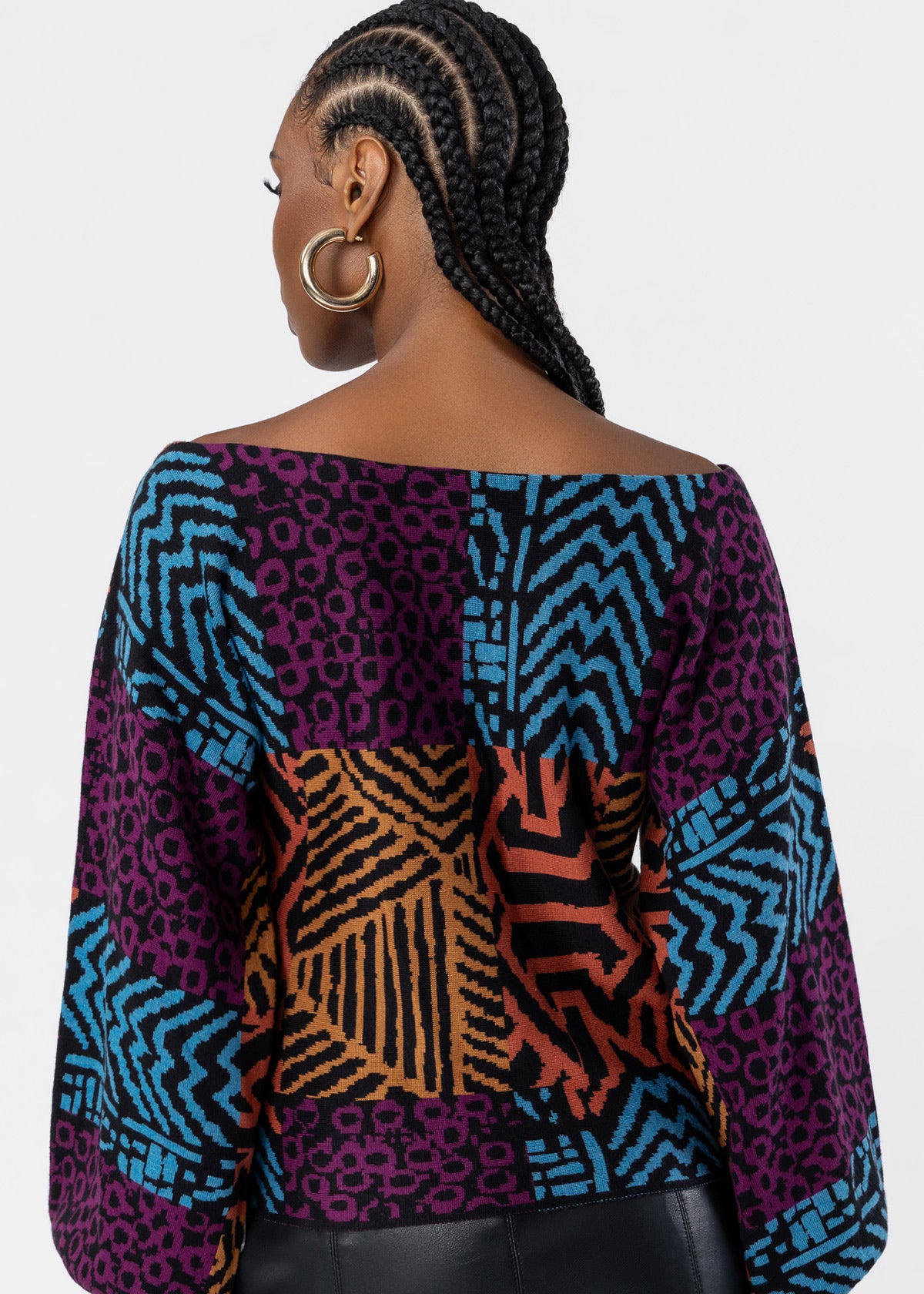 A woman shown from the back wearing a colorful patchwork-patterned top with wide sleeves. The top features geometric and animal-print panels in purple, blue, orange, black, and pink.