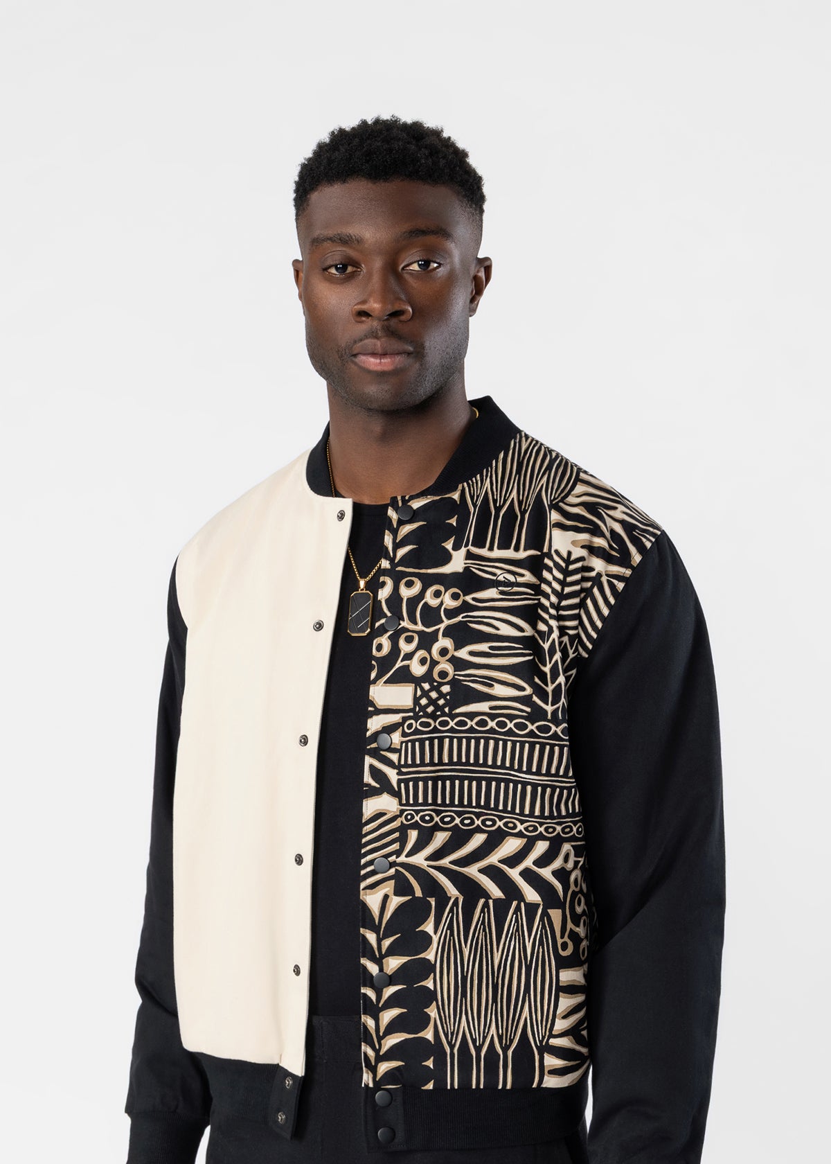 A man wearing a black and cream varsity-style jacket with a detailed botanical pattern on the right side, photographed against a light gray studio background.